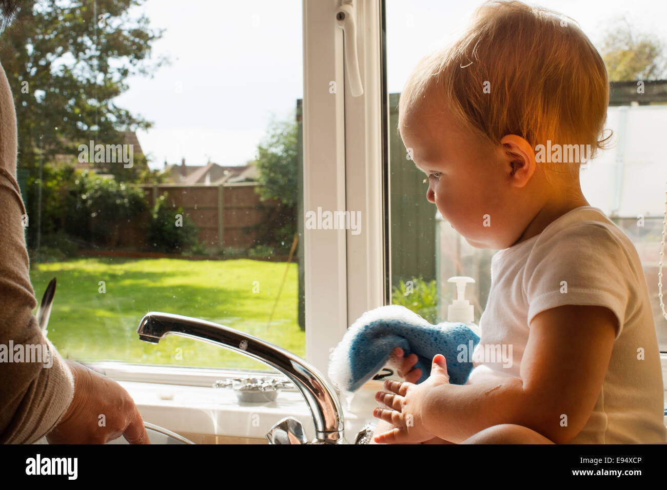 Bebé jugando con el agua en la cocina. Foto de stock