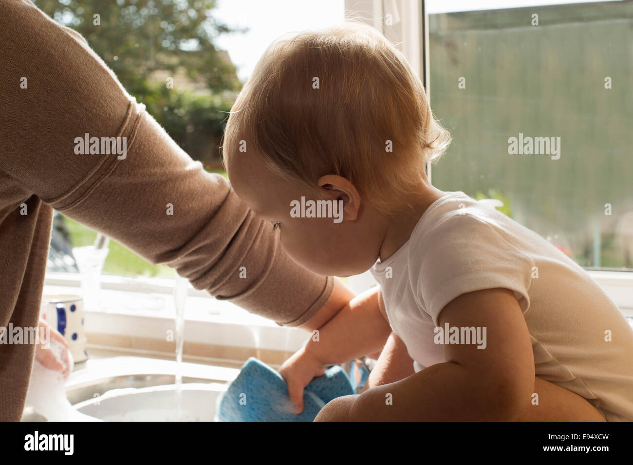 Bebé jugando con el agua en la cocina. Foto de stock