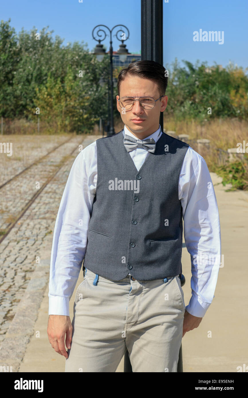 Hombre en camisa y chaleco con pajarita y gafas, de pie, apoyada contra una  farola en el antiguo vintage park o la ciudad y buscando Fotografía de  stock - Alamy