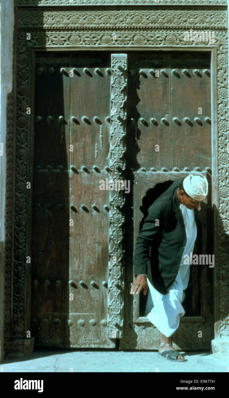 Una pequeña puerta dentro de una gran puerta de teca con un hombre saliendo tomado en Muscat en 1975, Sultanato de Omán Foto de stock