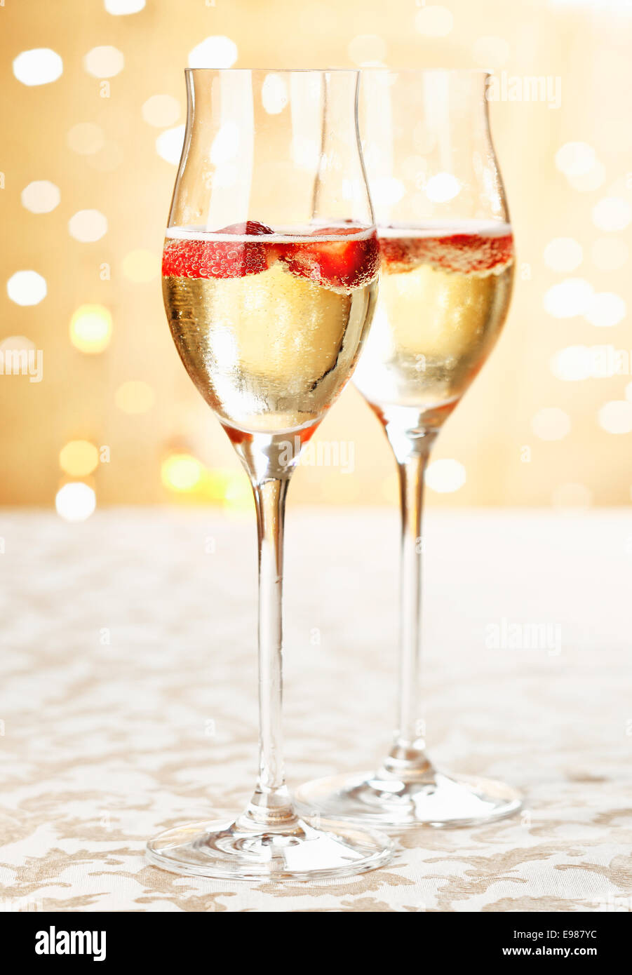 Copas de champaña festivo lleno de vino espumoso y fresas flotante con un telón de fondo bokeh de centelleo romántica parte Foto de stock