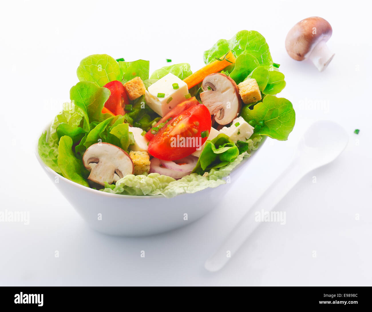 Lado individual sirve en un plato de china blanca fresca ensalada verde mixta con rodajas de champiñones frescos, tomate y queso feta. Foto de stock