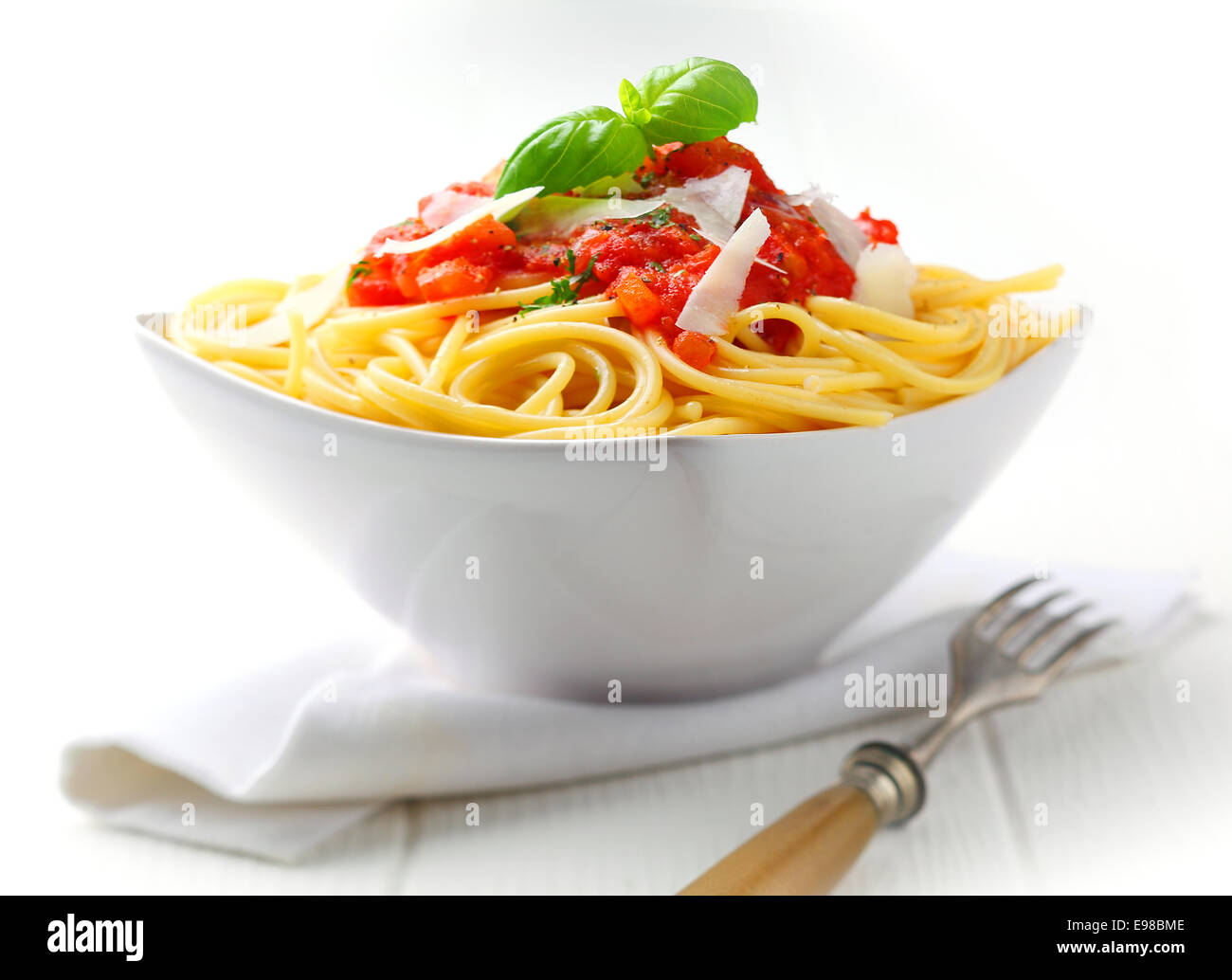 La pasta en un recipiente blanco con salsa de tomate y albahaca fresca con una servilleta blanca en un cuadro blanco. Foto de stock