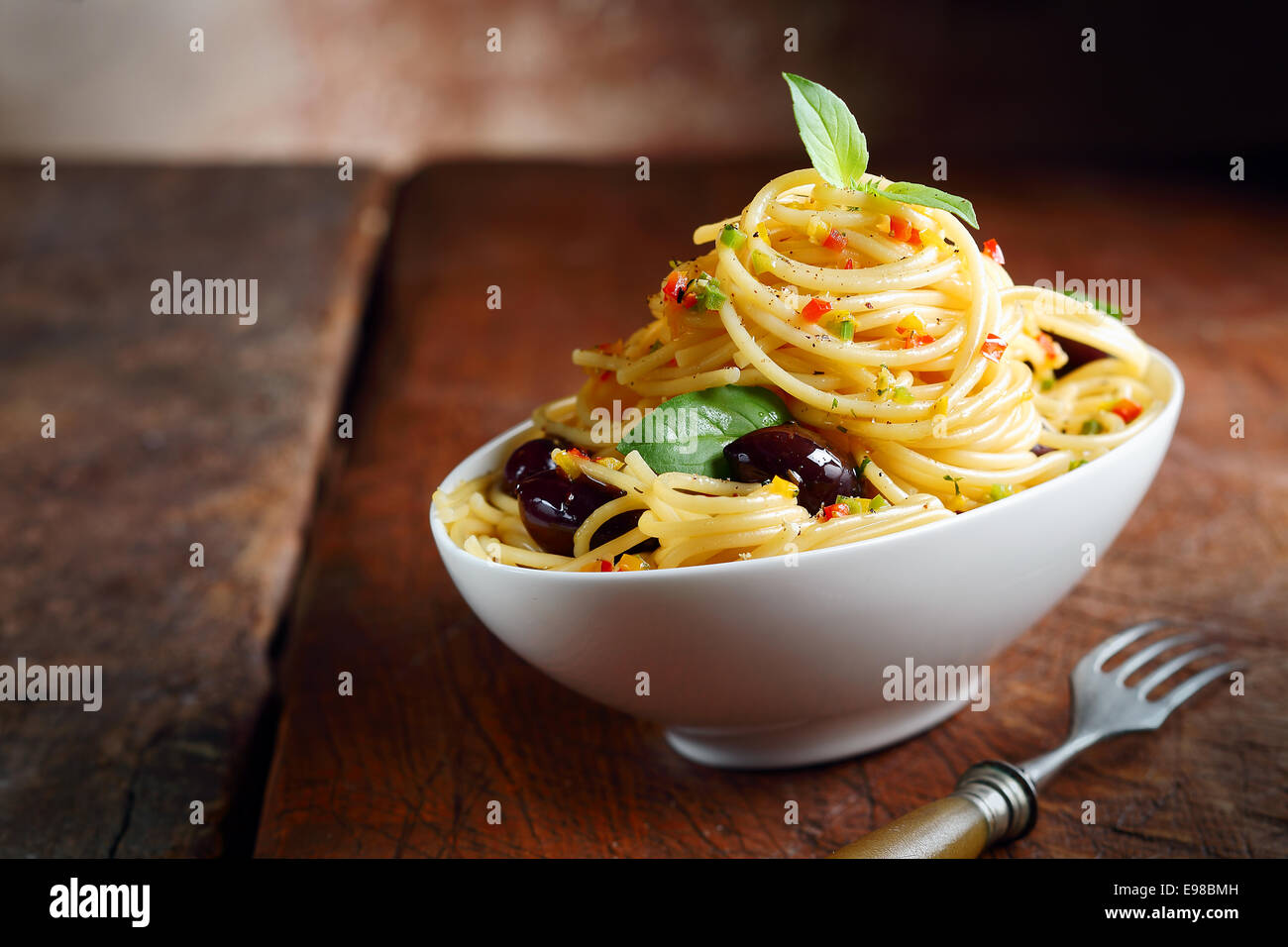 Espaguetis pasta en un recipiente blanco con aceitunas en una mesa de madera oscura. Foto de stock