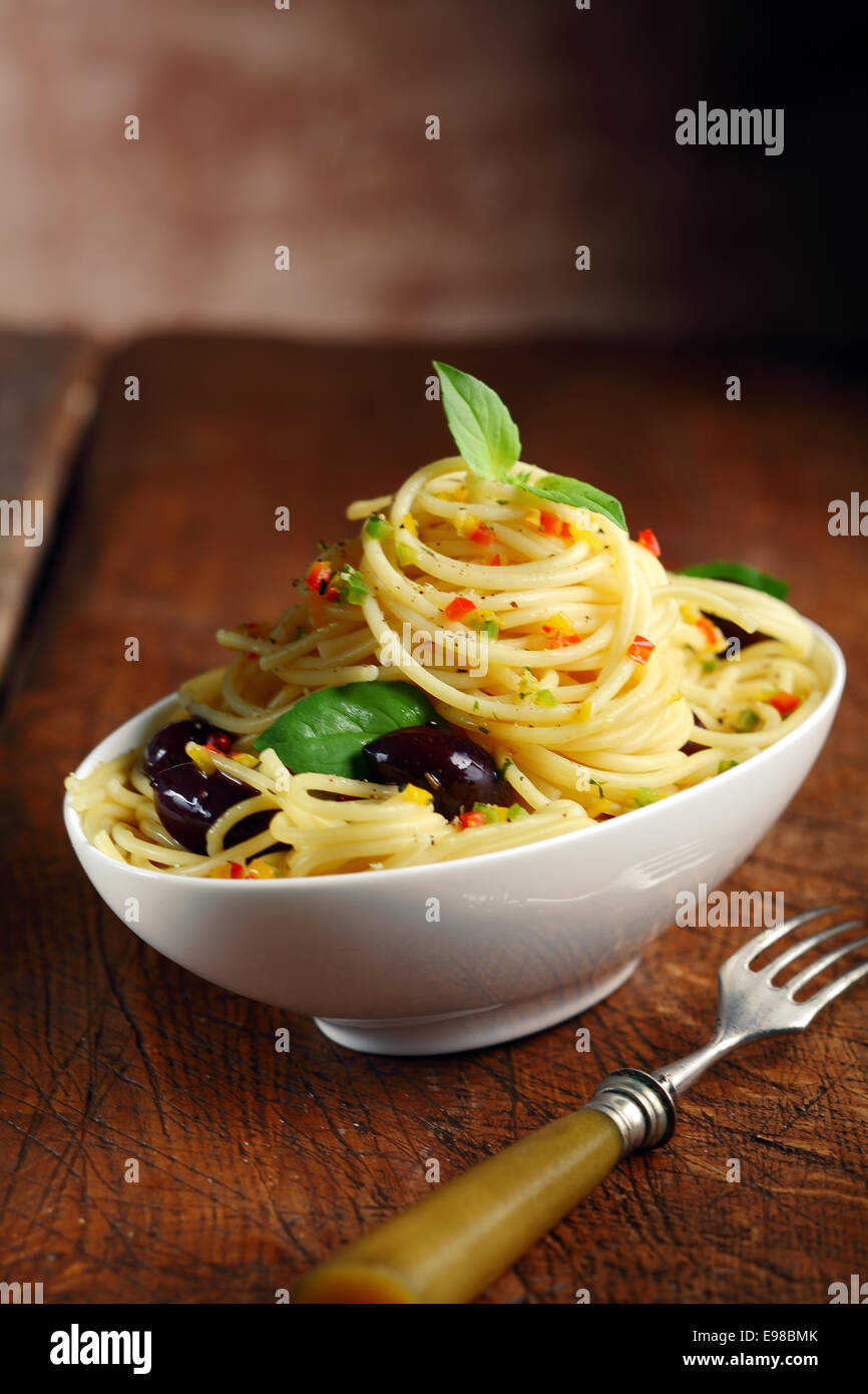 Espaguetis pasta en un recipiente blanco con aceitunas y horquilla en una mesa de madera oscura. Foto de stock