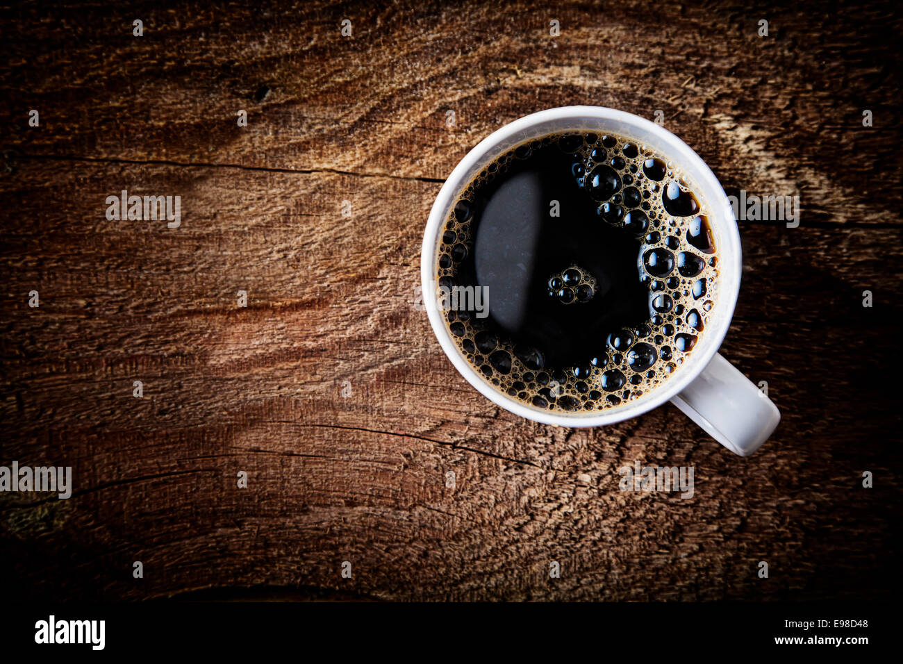Cerrar vista aérea de una espumosa taza de fuerte café espresso en una superficie de madera con textura rugosa viñeteado oscuro y un resaltado alrededor de la taza, con copyspace Foto de stock