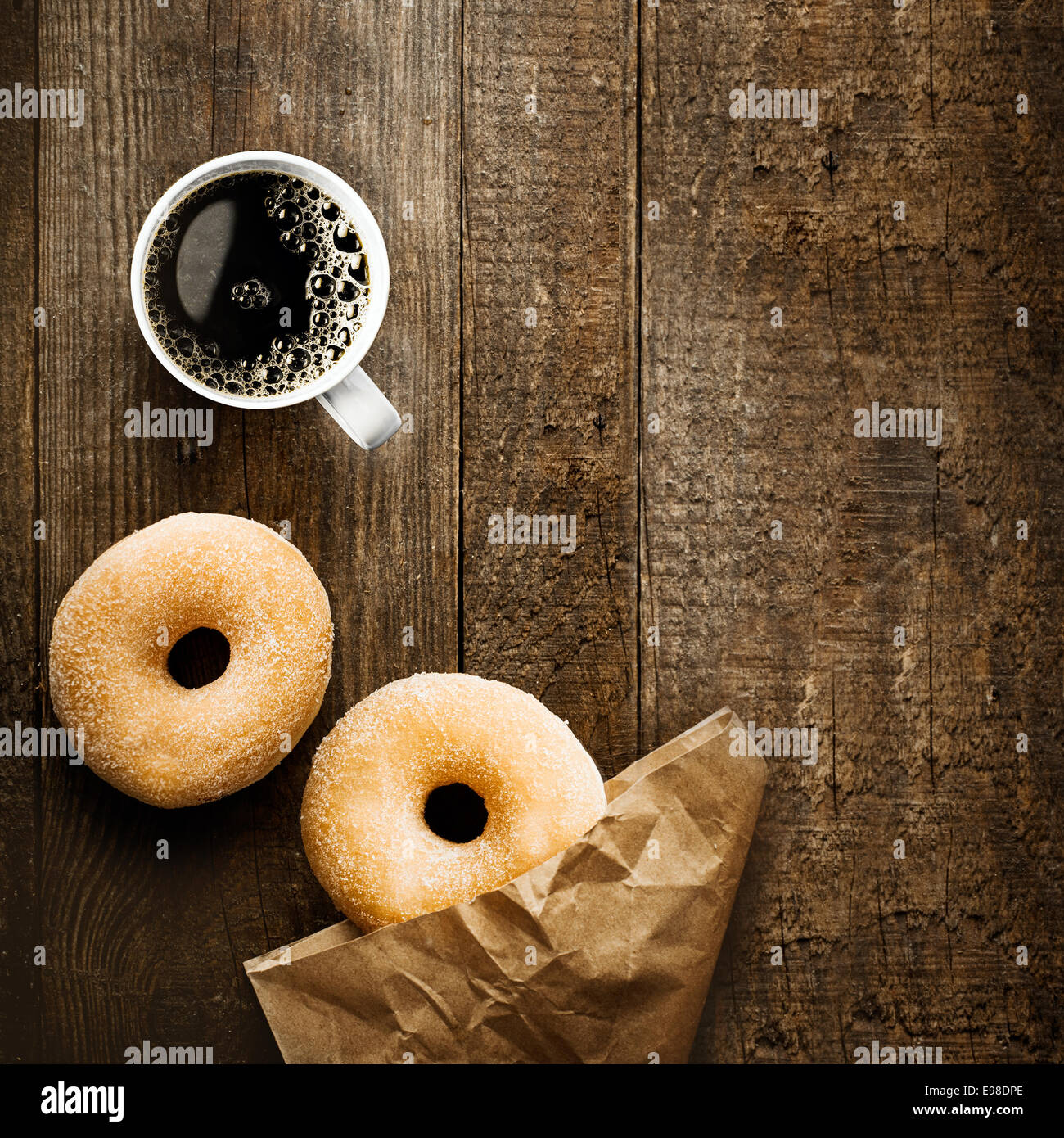 Cerrar vista aérea de dos deliciosos donut anillo azucaradas con café espresso y arrugado paquete de papel marrón sobre una superficie de madera rústica con copyspace para una relajante pausa café Foto de stock