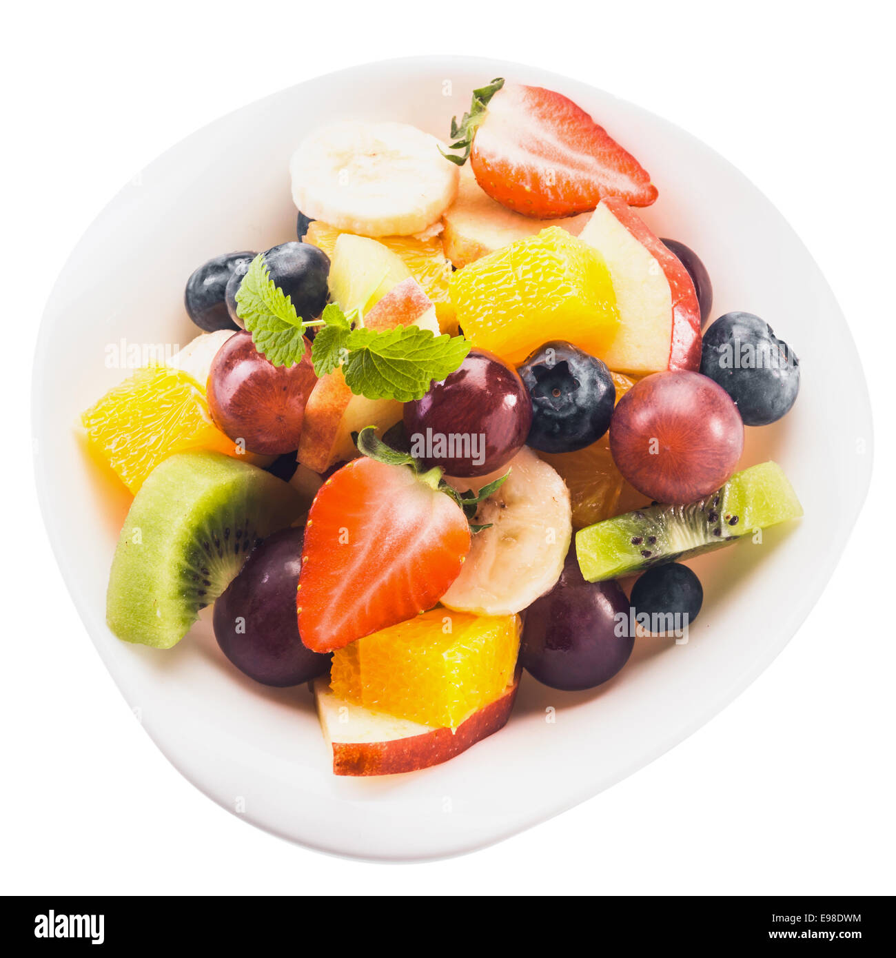 Cerrar vista desde arriba de la ensalada de frutas tropicales frescas en un recipiente con trocitos de kiwi, manzana, naranja, uva, plátano, fresas y arándanos, aislado en blanco Foto de stock