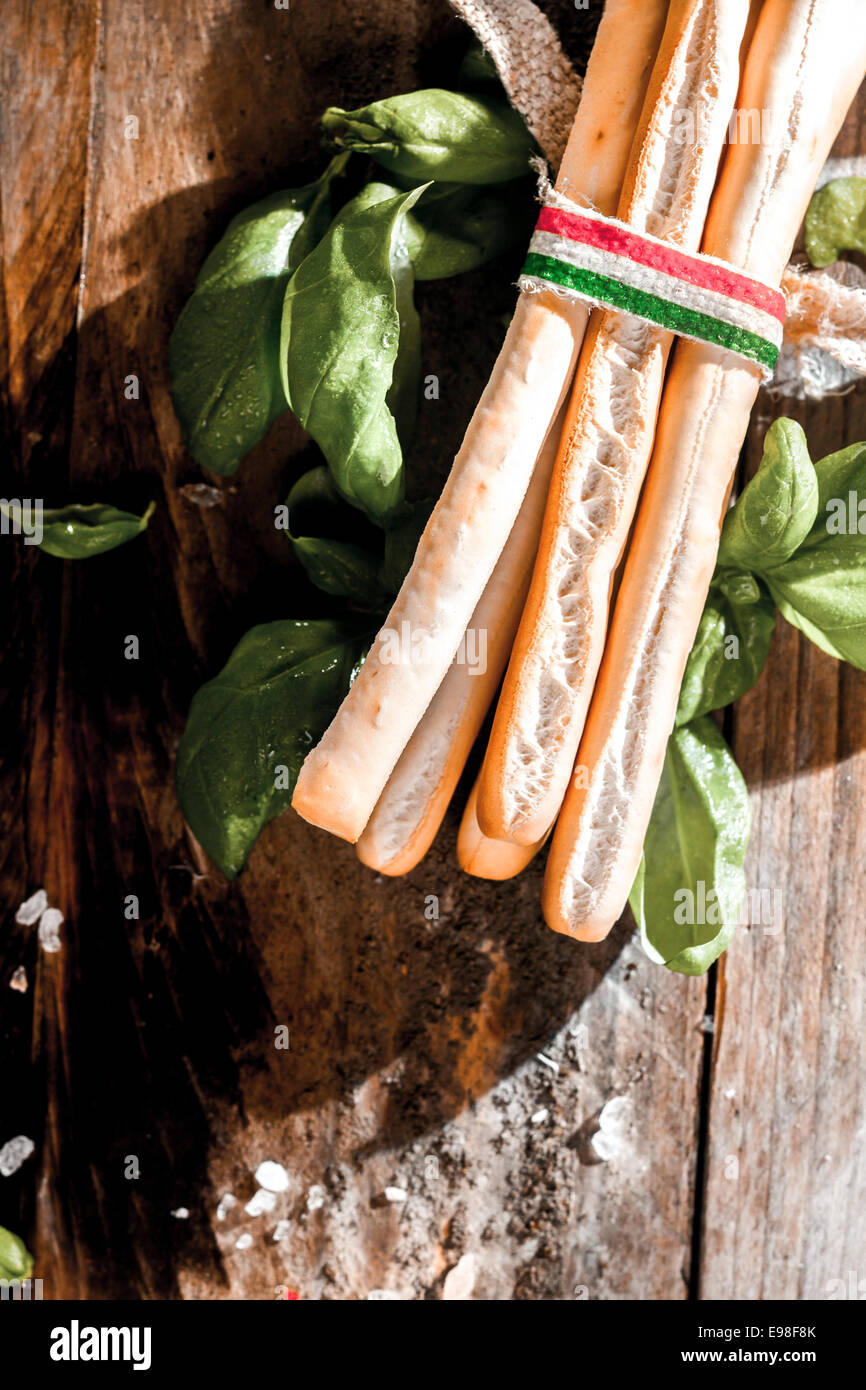 Crujientes grissini Bread Sticks, un tradicional pan italiano delgado y largo tubo de pasta sin levadura, con albahaca fresca sobre una tabla de madera rústica, vista superior Foto de stock