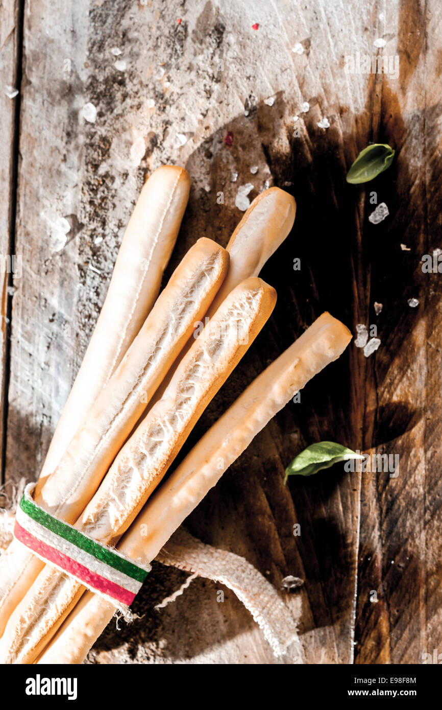 Grissini palos de pan italiano hechas de oro crujiente masa sin levadura de la harina cocida, atado en un paquete con una cinta con los colores de la bandera nacional italiana acostado sobre una mesa de madera rústica grunge Foto de stock