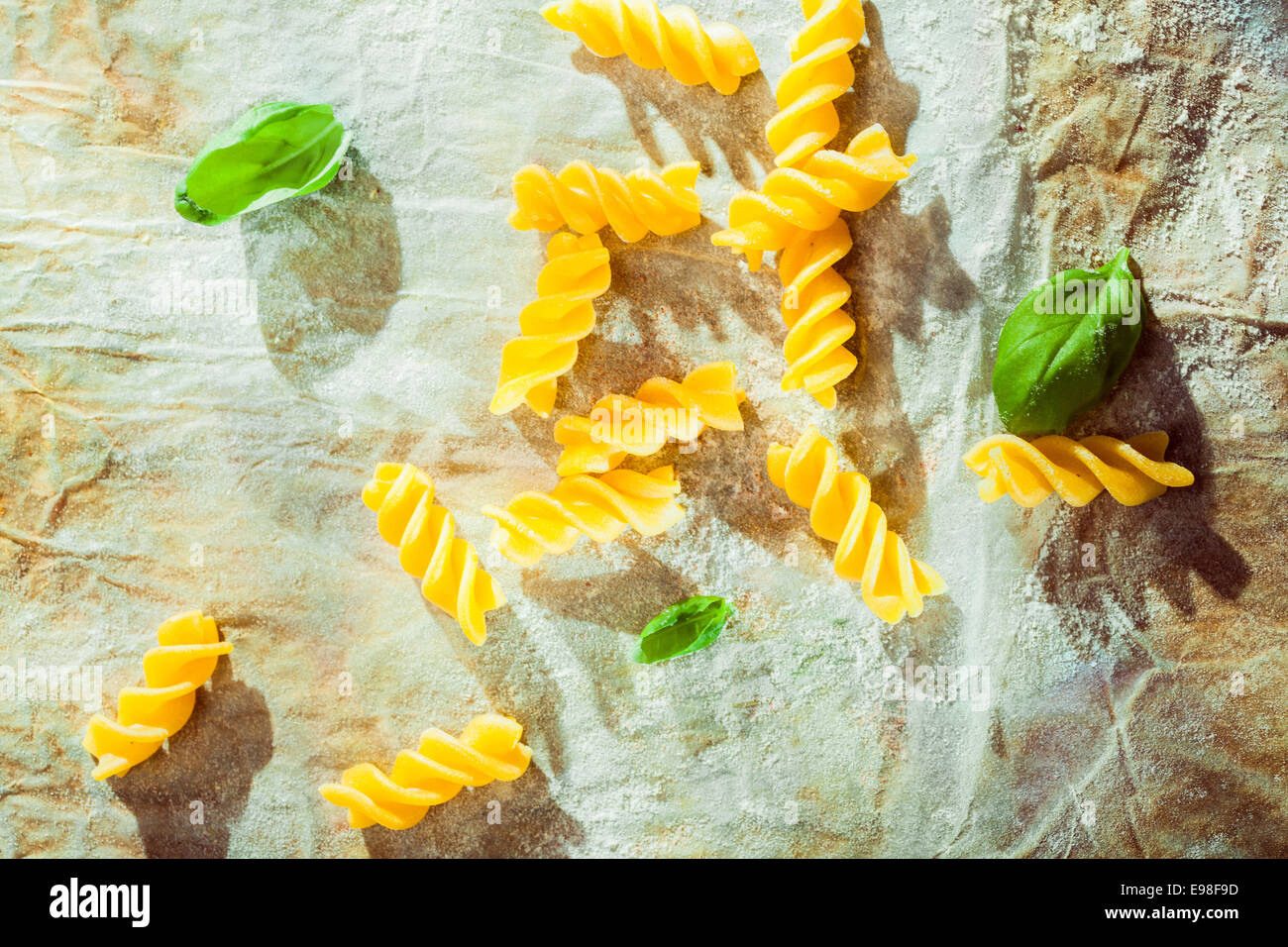 Vista aérea de la espiral fusilli pasta con hojas de albahaca fresca utilizada como ingrediente en la cocina tradicional italiana en arrugado papel sucio Foto de stock