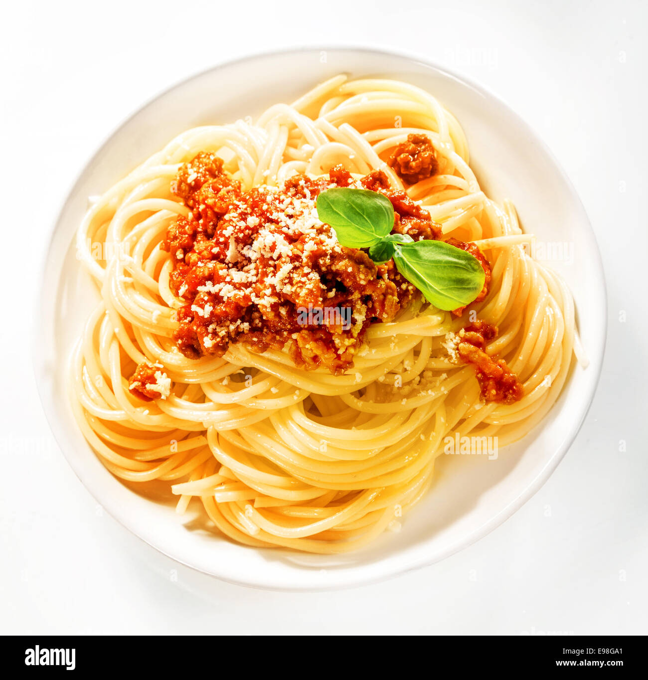 Sirviendo de italiano espaguetis con carne y salsa de tomate espolvoreada con queso parmesano rallado y adornado con hojas de albahaca fresca, vista desde arriba Foto de stock