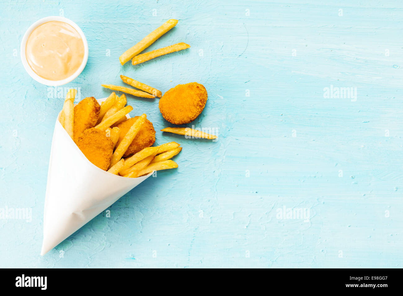 Vista aérea sobre un fondo azul con copyspace medallones de pescado frito y patatas fritas en un cono de papel para llevar con mayonesa sabrosa dip Foto de stock