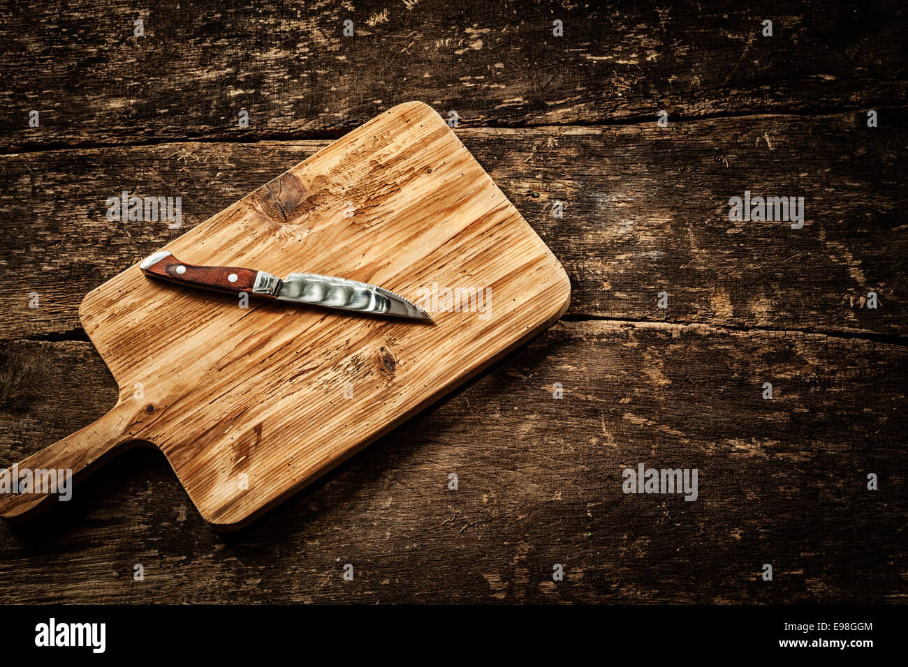 Vaciar tabla de cortar con un cuchillo para pelar bien afilado sobre una mesa de madera grunge angustiado en una rústica cocina, vista aérea con una viñeta y copyspace Foto de stock