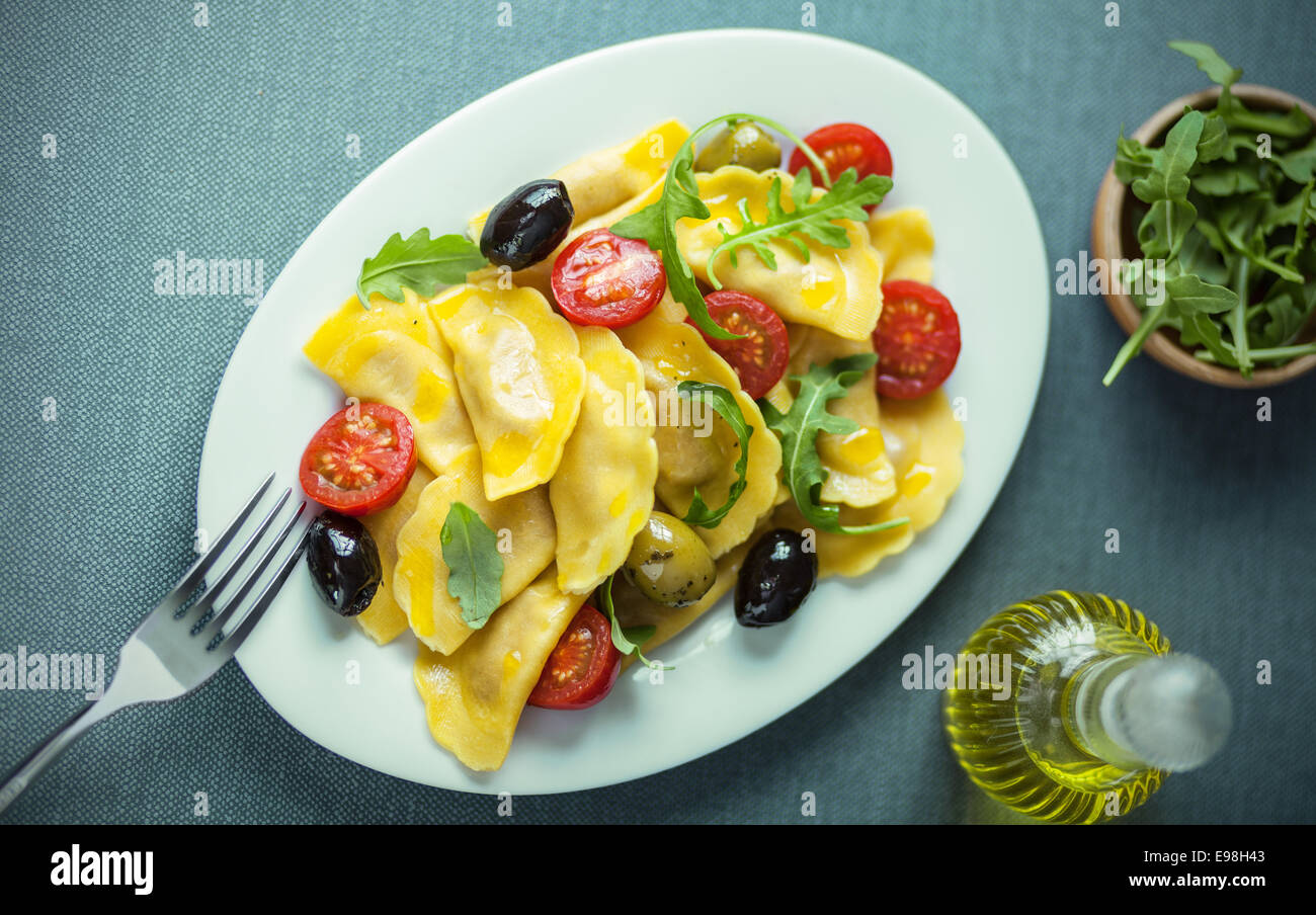 Ravioli italiano con ensalada de rúcula o cohete fresca, tomates cherry y aceitunas aderezadas con aceite de oliva virgen, vista desde arriba Foto de stock
