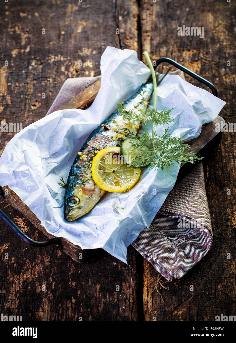 Una deliciosa cena de marisco de pescado entero al horno con un condimento de surtido de hierbas frescas, limón y especias, vista desde arriba sobre una encimera de madera rústica Foto de stock