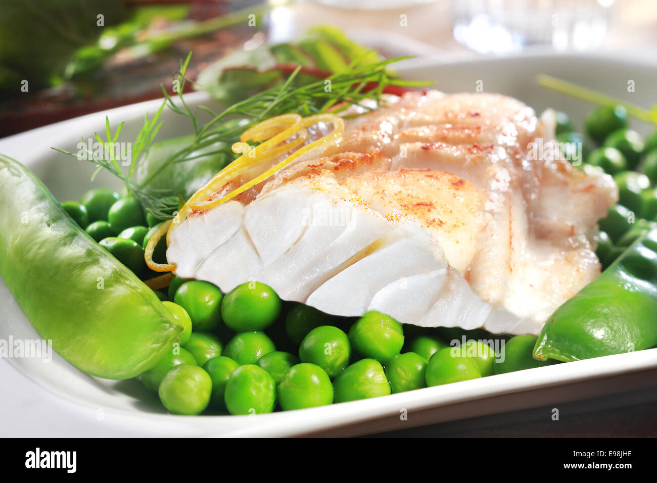 Filete de pescado a la parrilla saludable con guisantes, mangetouts la ralladura de limón y sirve en un plato como aperitivo o plato principal Foto de stock