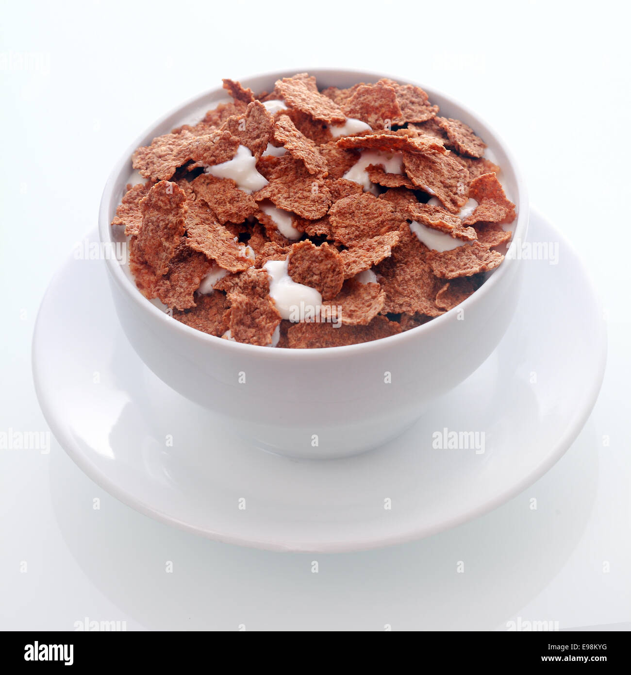 Tazón de crujientes hojuelas de cereal de desayuno con sabor de chocolate de leche para una sabrosa comida nutritiva servida en un cuenco de cerámica blanca y platillo , en formato cuadrado Foto de stock
