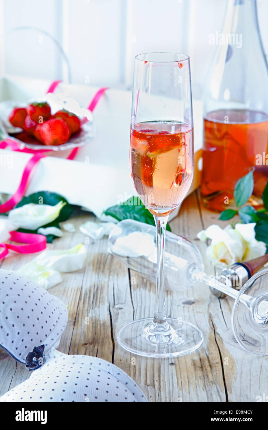 Champagne llena con champán rosado y trozos de fresa sobre un tratamiento decorativo de mesa, después de una celebración o una fiesta Foto de stock