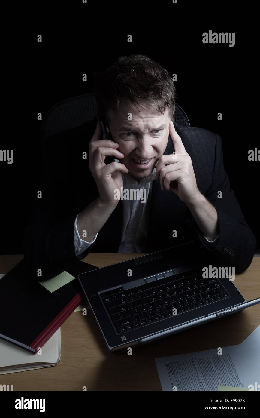 Imagen vertical de hombre de negocios, expresar el enojo, mientras que en su teléfono celular, trabajando tarde con fondo negro Foto de stock