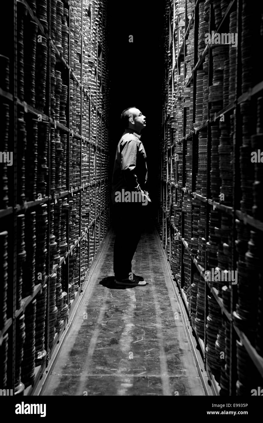 Retrato del miembro masculino del personal en el BFI con estantes llenos de rollos de película / caja de cartones de cine clásico Foto de stock