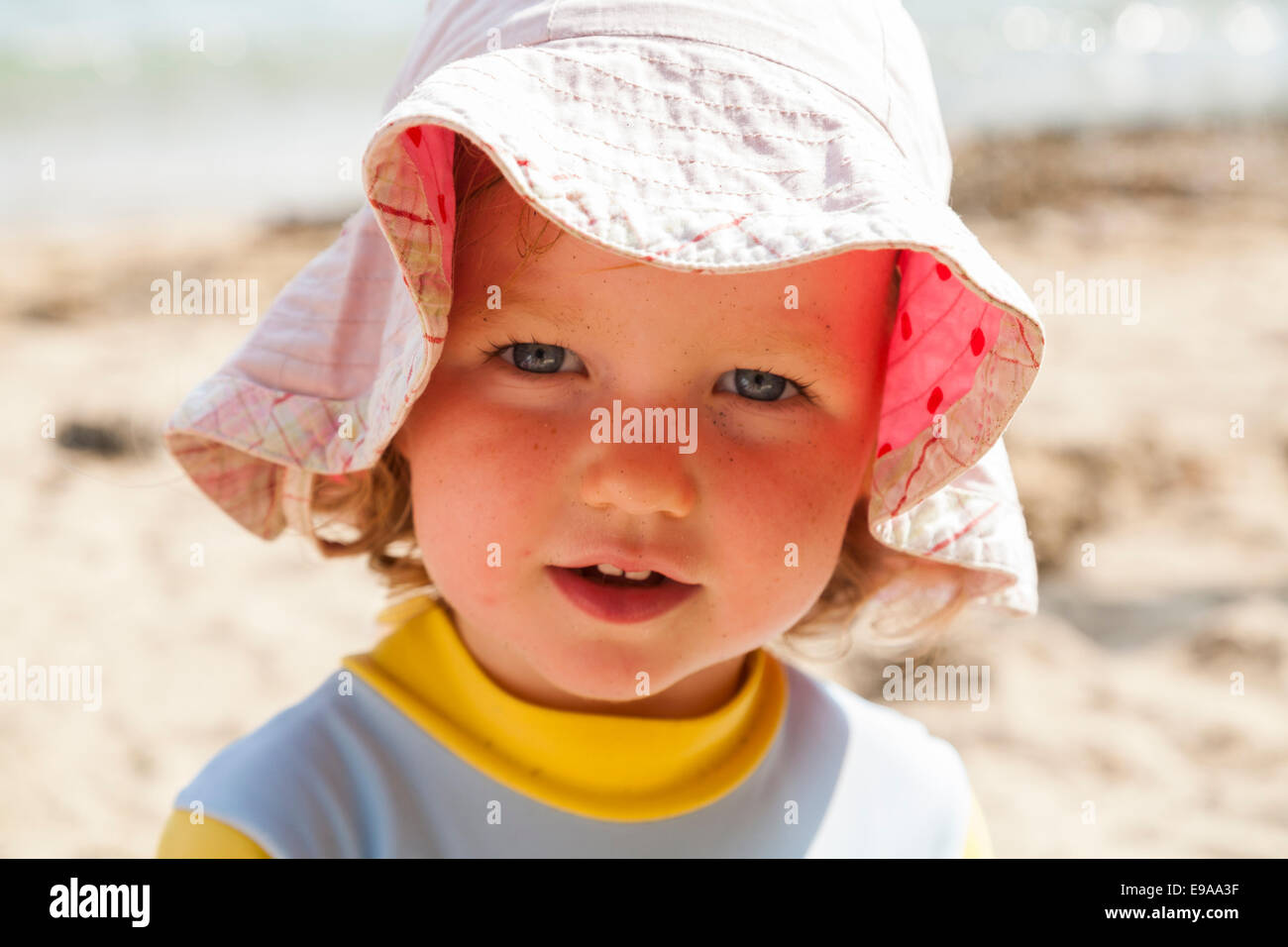 Sonrisa dos sonriente niño de 2 años, niño niña cubierto por sombrero para el sol y playa con ropa diseñada para proteger del sol. Vacaciones en el Reino Unido Cornwall