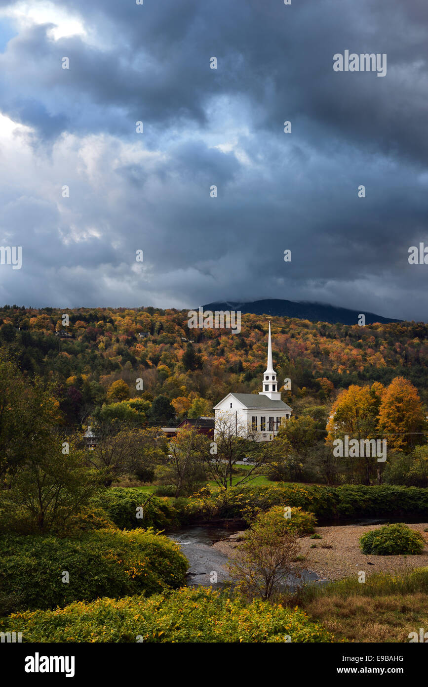 Nubes oscuras sobre Stowe iglesia comunitaria contra la caída de color en la colina de pincel con río Waterbury Stowe, Vermont, EE.UU. Foto de stock