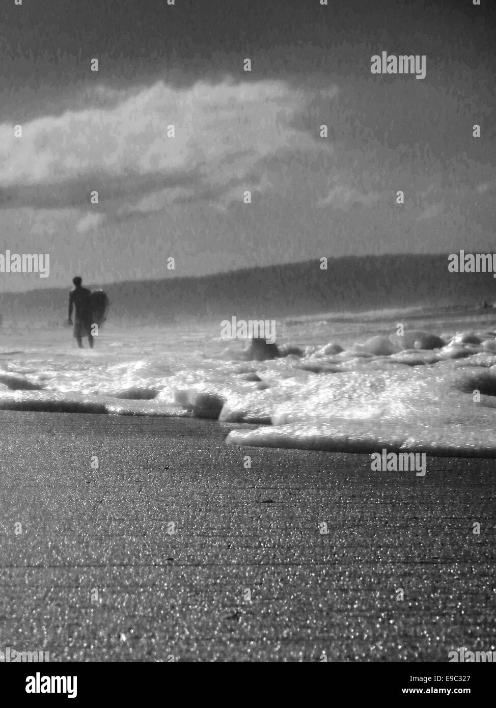 Surfer caminar fuera del océano con agua corriendo hasta la arena Foto de stock