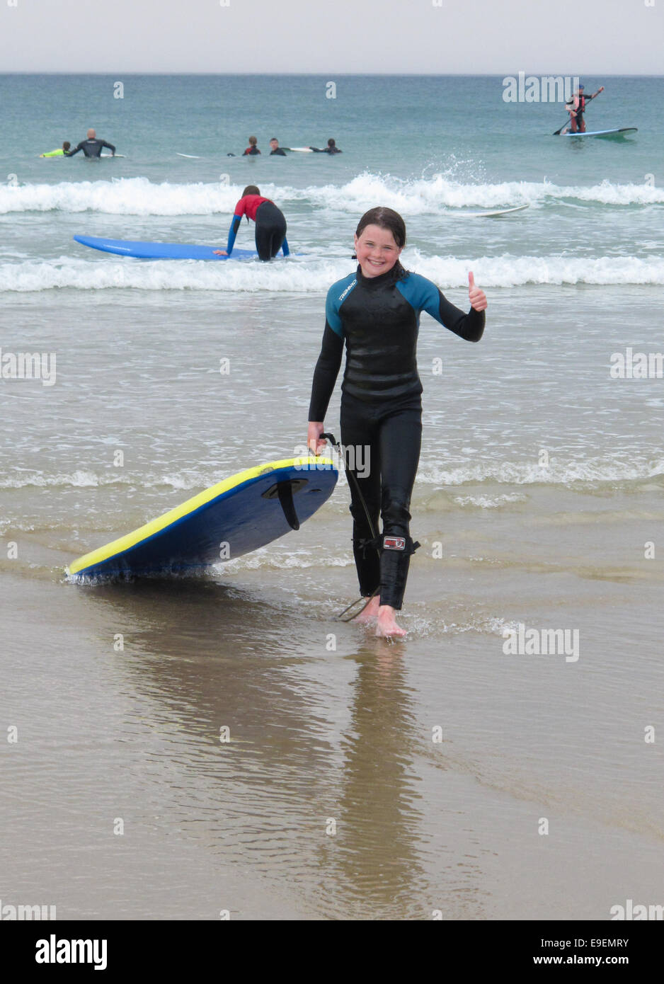 Conexión diario Limpiar el piso Niña arrastrando su tabla de surf en la playa mar después de una sesión de  surf, UK Ella lleva un traje de neopreno, sonriente y está haciendo un  pulgar hacia arriba Fotografía