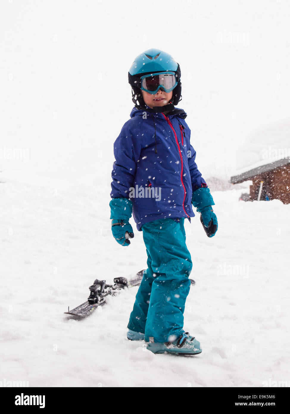 Pequeño niño en ropa de esquí, cascos y gafas, listo para ir a esquiar con  la caída de nieve Fotografía de stock - Alamy