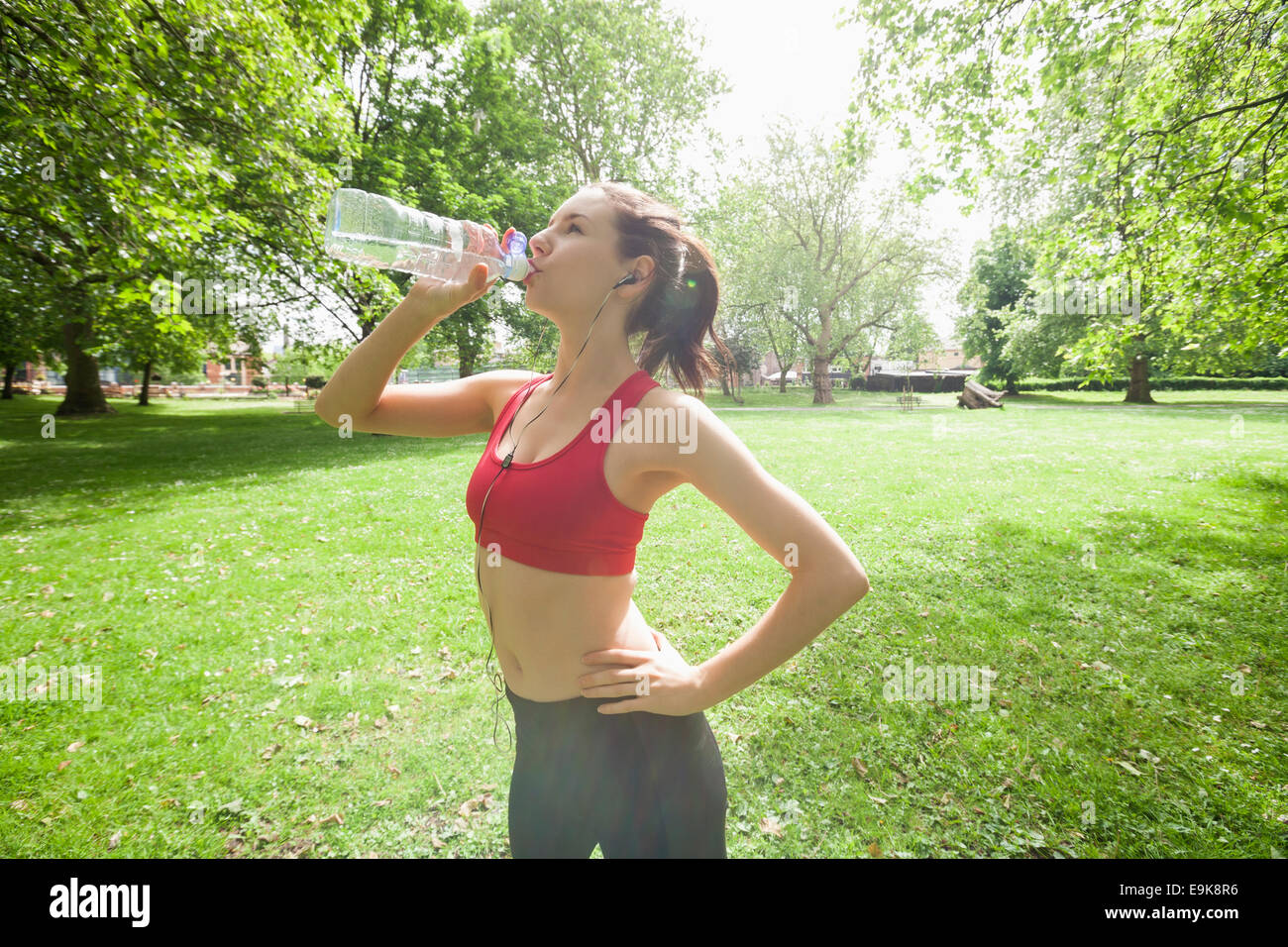 Colocar mujer agua potable mientras escucha música en el parque Foto de stock