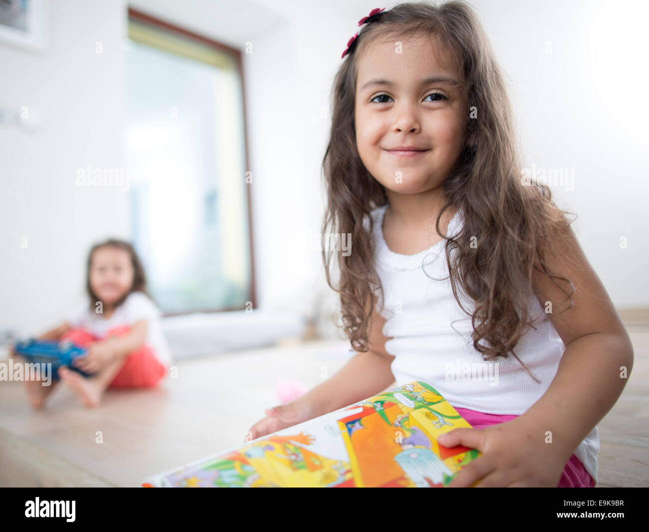 Retrato de linda chica sujetando libro con su hermana en el fondo en el hogar Foto de stock