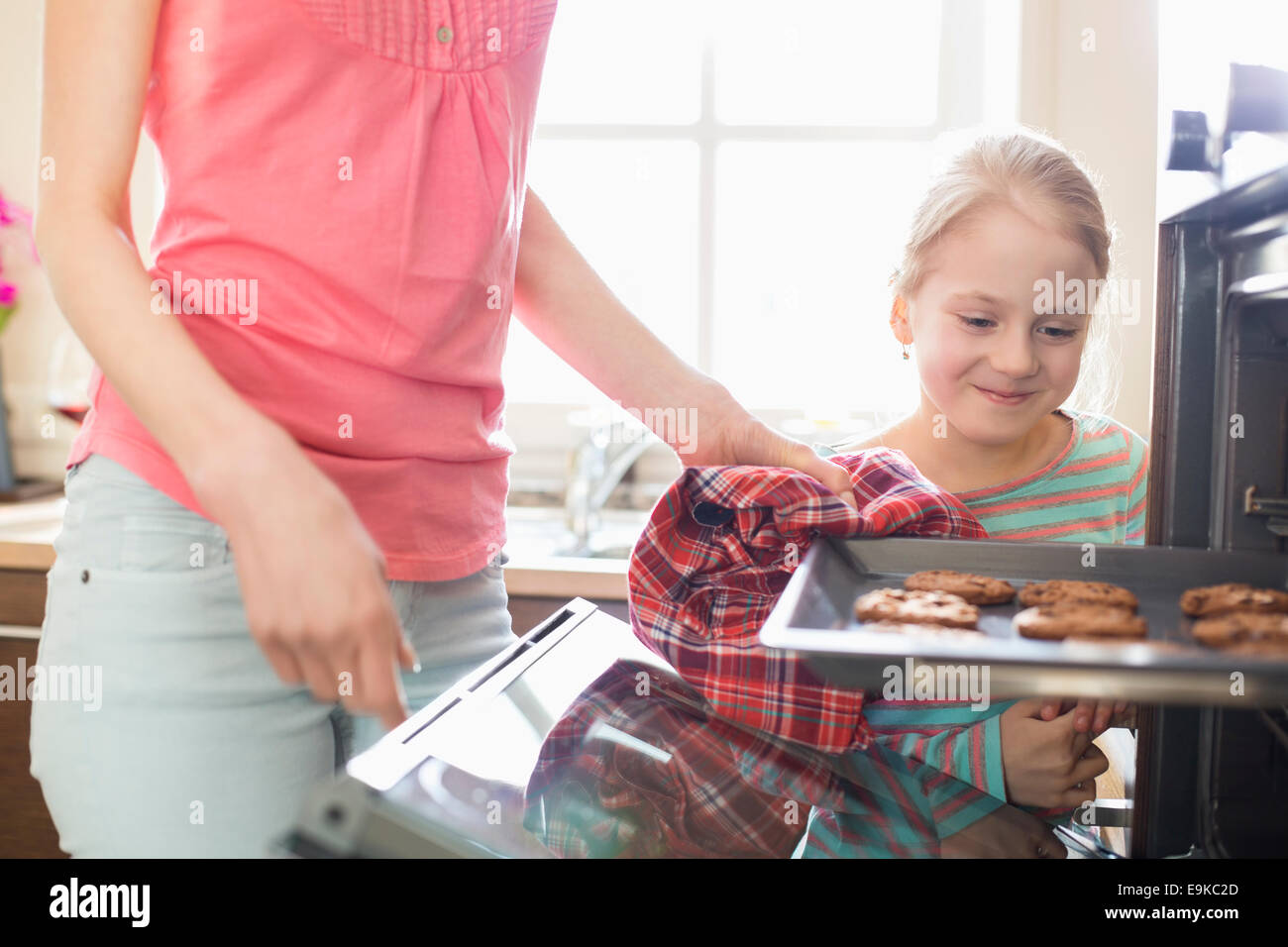 Sonriendo mirando a la madre eliminar cookie la bandeja del horno en casa Foto de stock