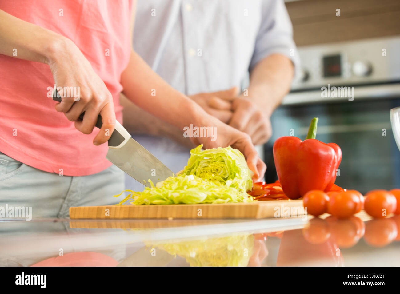 La mitad del torso de mujer picar las verduras en la cocina con el hombre de pie en segundo plano. Foto de stock
