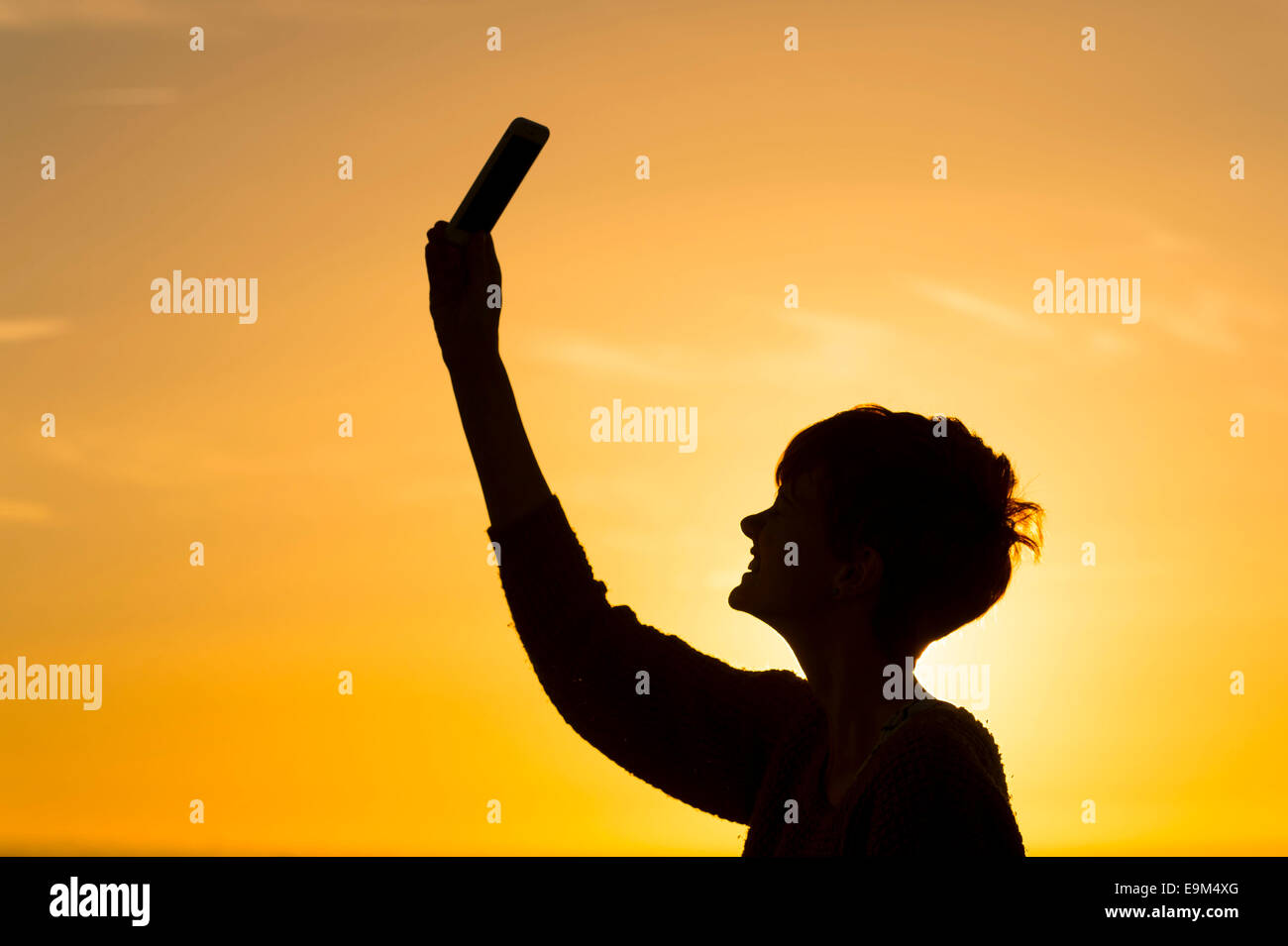 Una silueta chica posee un teléfono móvil en el aire para tratar de recibir una señal de datos. Foto de stock