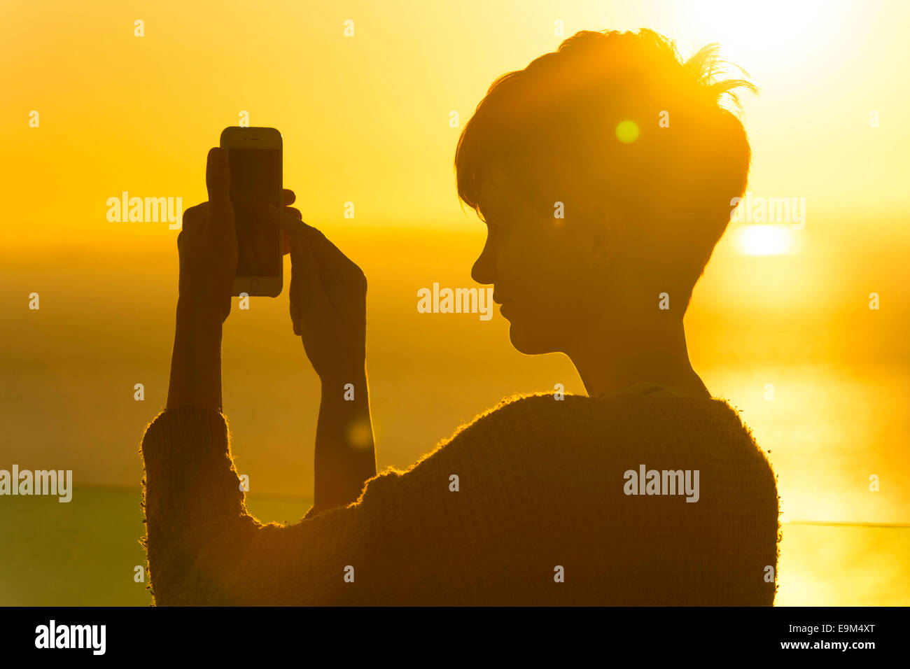 Una mujer usa un teléfono móvil en una red de roaming extranjeros mientras se encuentra de vacaciones durante la puesta de sol del amanecer. Foto de stock