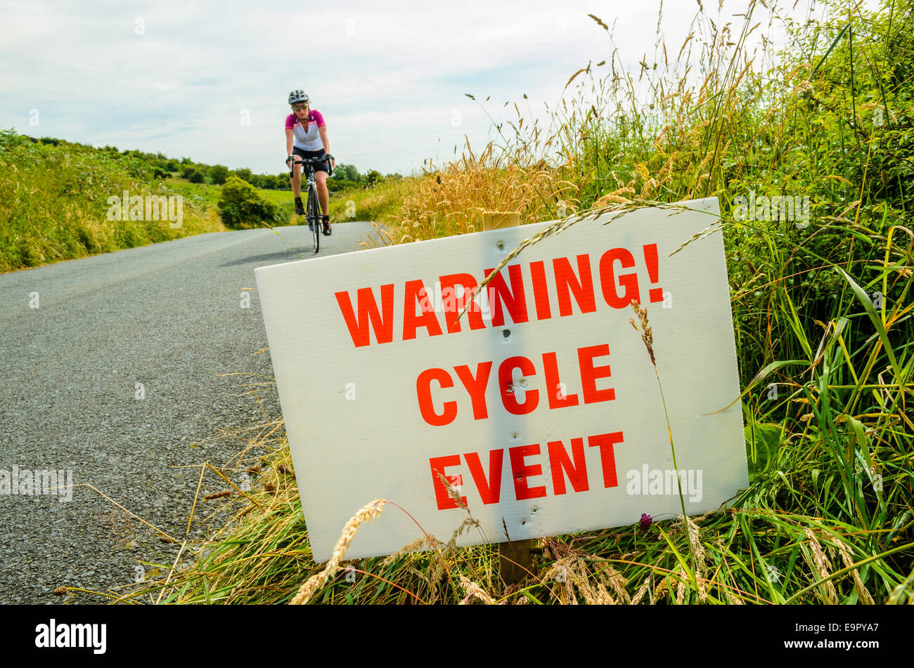 Ciclista y señal de advertencia sobre la tranquila carretera en Cumbria Foto de stock