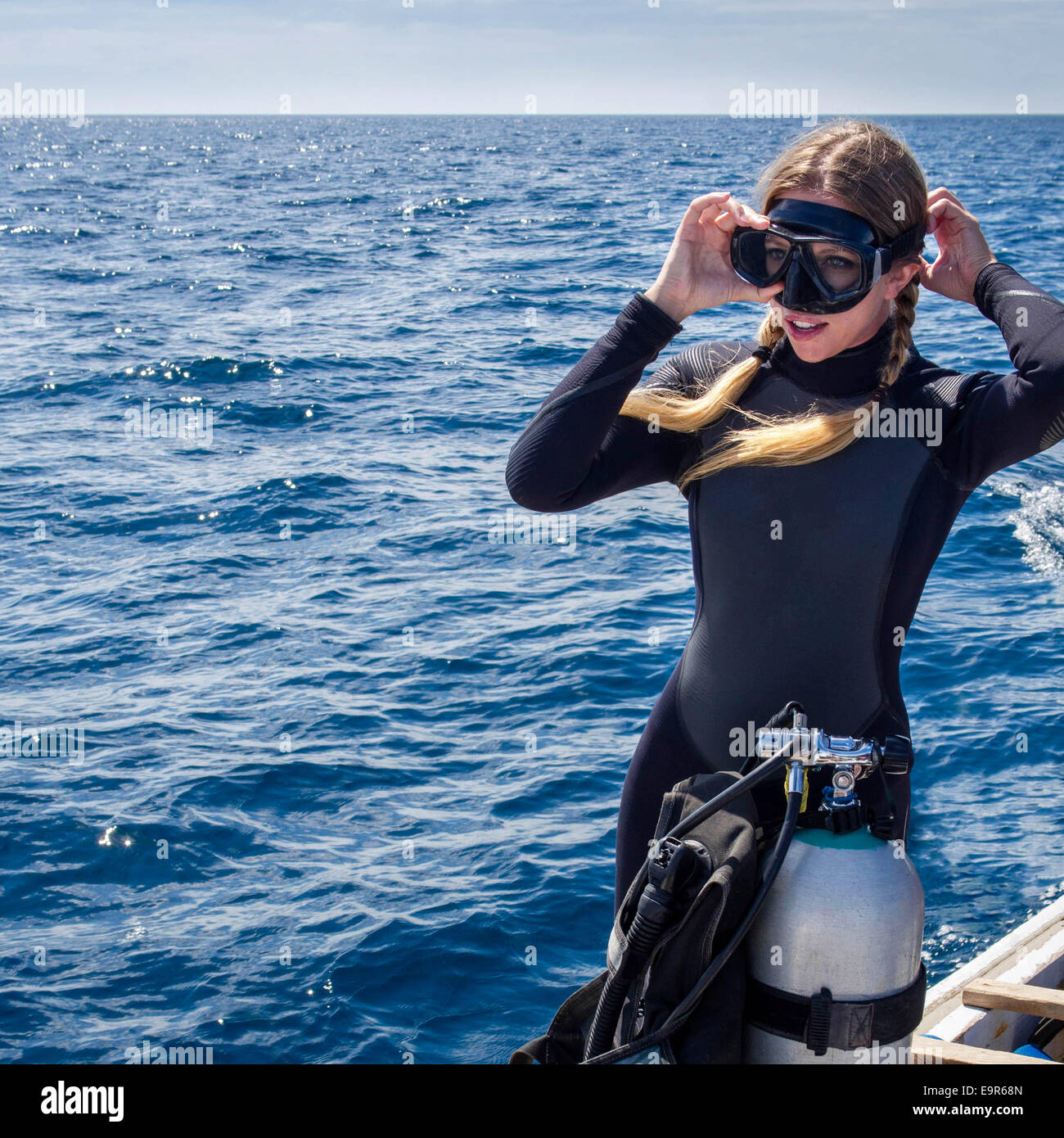 Mujer caucásica en traje de neopreno en un barco poniendo sobre gafas en preparación para la práctica del submarinismo. Foto de stock