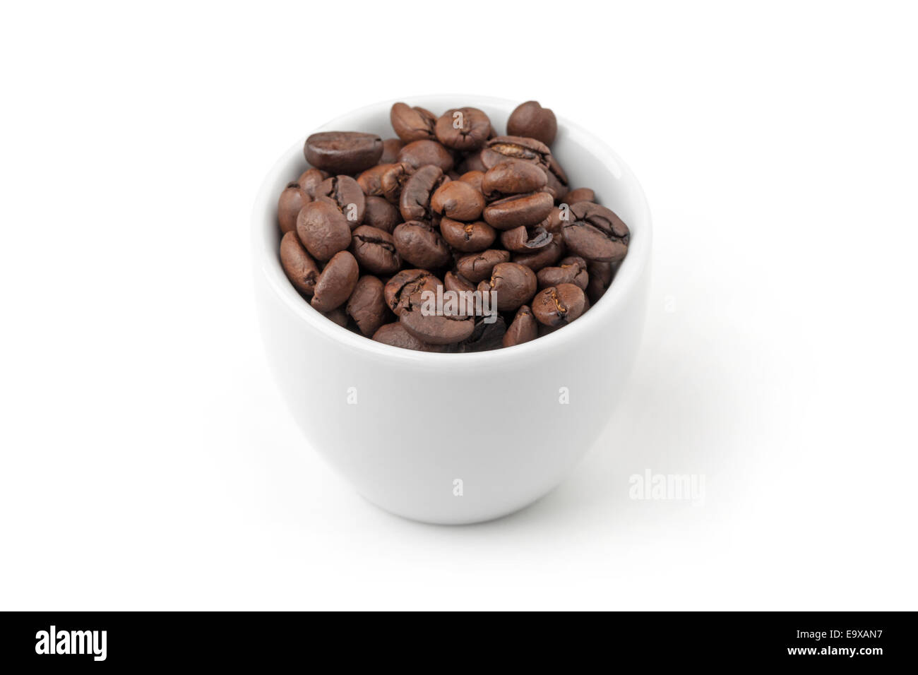 Taza de café blanco pequeño lleno de granos de café tostado fresco sobre fondo blanco, el enfoque selectivo Foto de stock