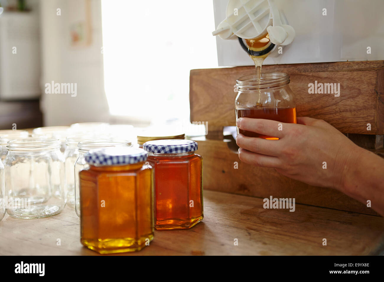 Mano de apicultor femenino en cocina embotellamiento miel filtrada de colmena Foto de stock
