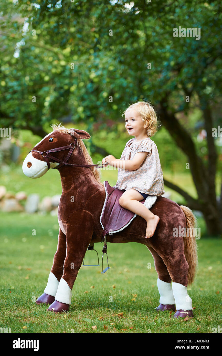 Retrato de niño hembra montando caballo de juguete en el jardín Foto de stock