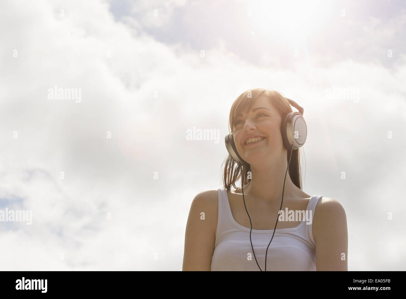 Mujer joven con los auriculares puestos bajo el cielo soleado Foto de stock