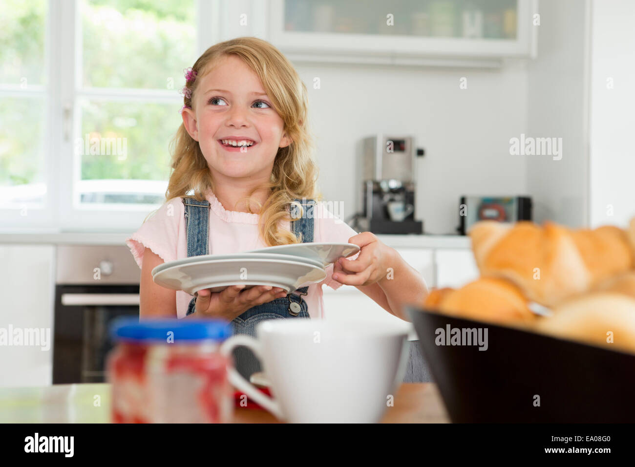Chica sujetando las placas y ajuste de la mesa de la cocina Foto de stock
