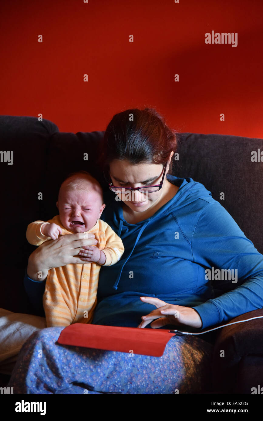 Una madre en pijama usando un ipad e ignorando su llanto del bebé Foto de stock