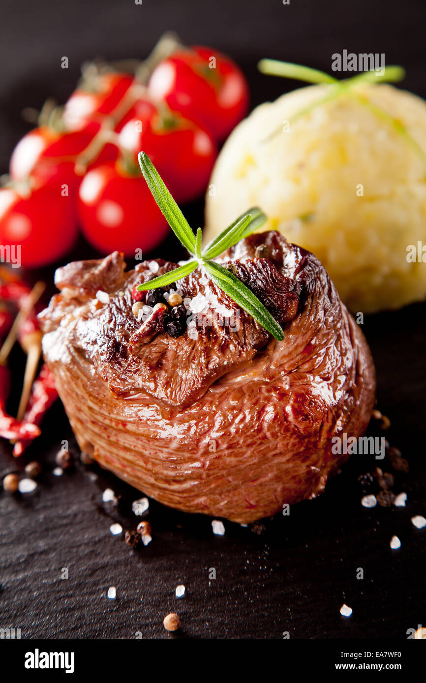 Trozo de carne roja de ternera con romero sirve de superficie de piedra negra. Foto de stock