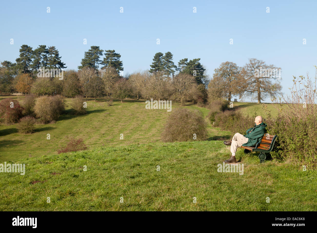 Un hombre sentado en un banco mirando a través de la campiña inglesa, Welcombe Hills, Warwickshire, REINO UNIDO Foto de stock