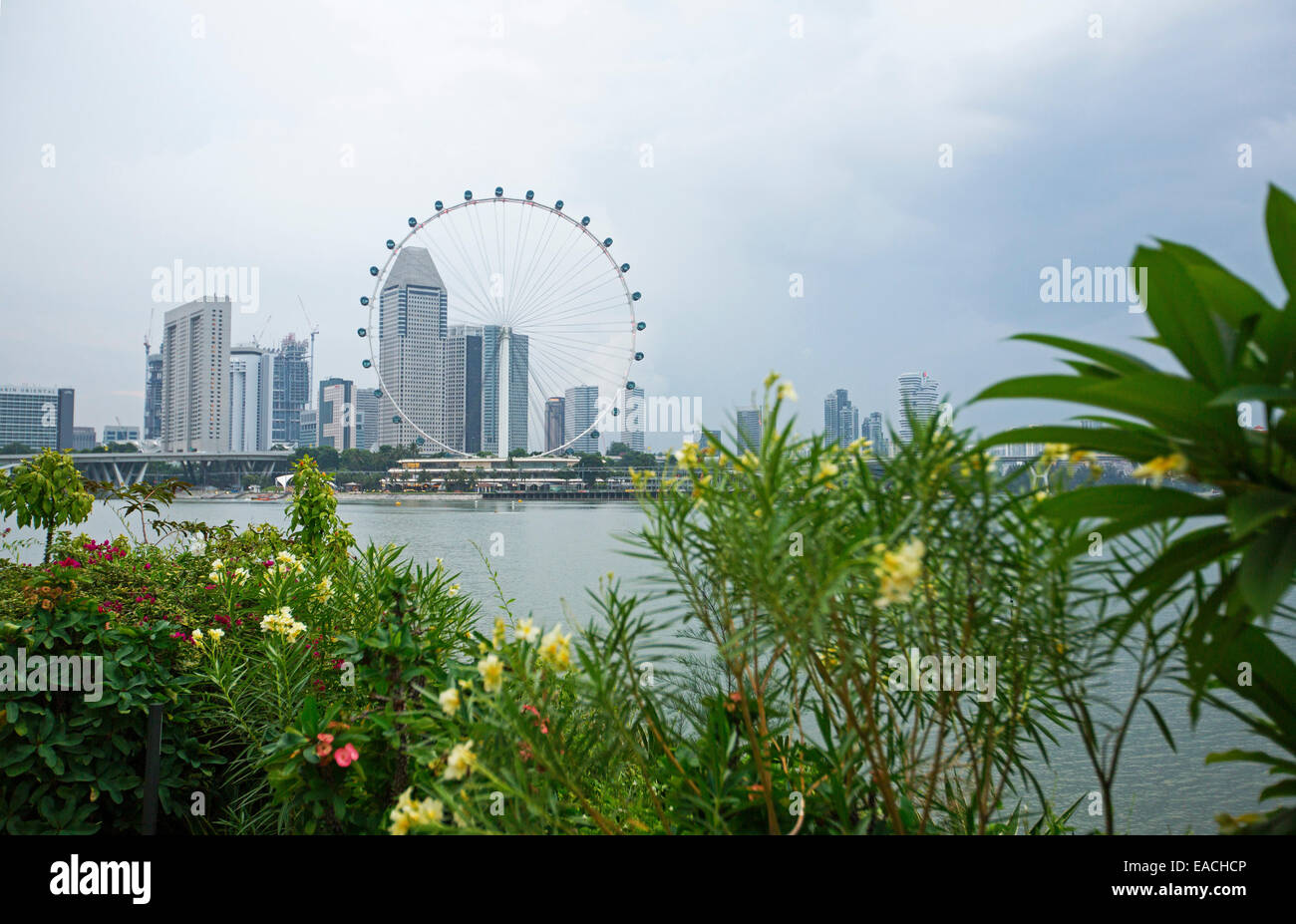 Vista de los rascacielos de la ciudad de Singapur con & enorme noria de observación junto a tranquilas aguas azules de la bahía Foto de stock