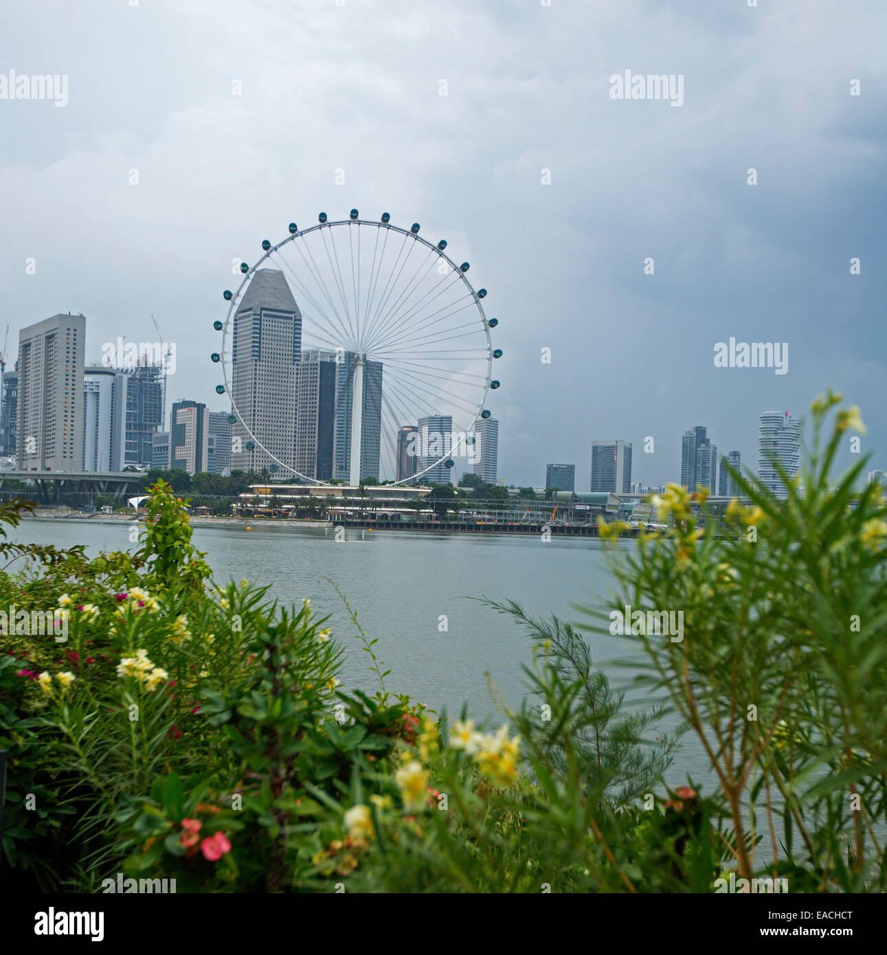 Vista de los rascacielos de la ciudad de Singapur con & enorme noria de observación junto a tranquilas aguas azules de la bahía Foto de stock