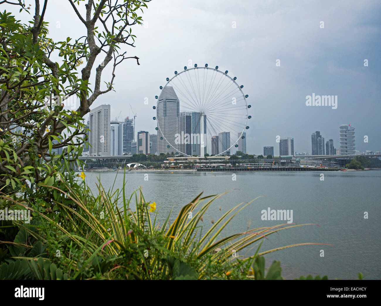 Vista de los rascacielos de la ciudad de Singapur con & enorme noria de observación junto a tranquilas aguas azules de la bahía Foto de stock