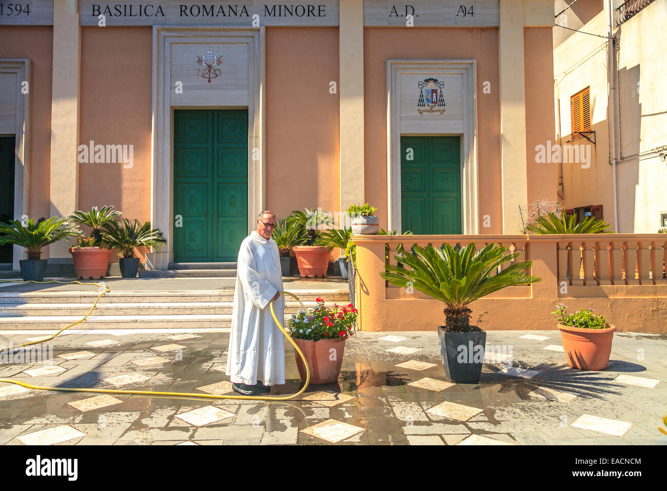 Un sacerdote de regar las plantas en frente de su iglesia en la ciudad de Lipari Foto de stock